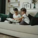 Young siblings engaged in reading on a sofa, showcasing comfort and togetherness in a home setting.